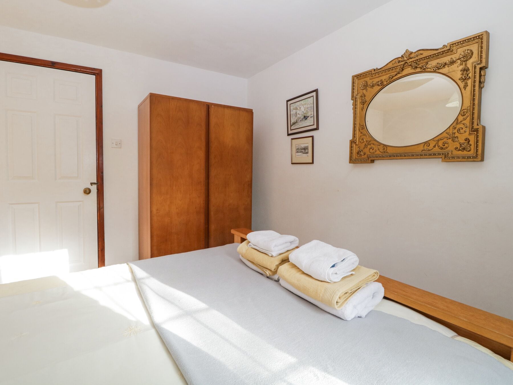 Una camera da letto con un letto, un armadio, uno specchio e due quadri appesi al muro.