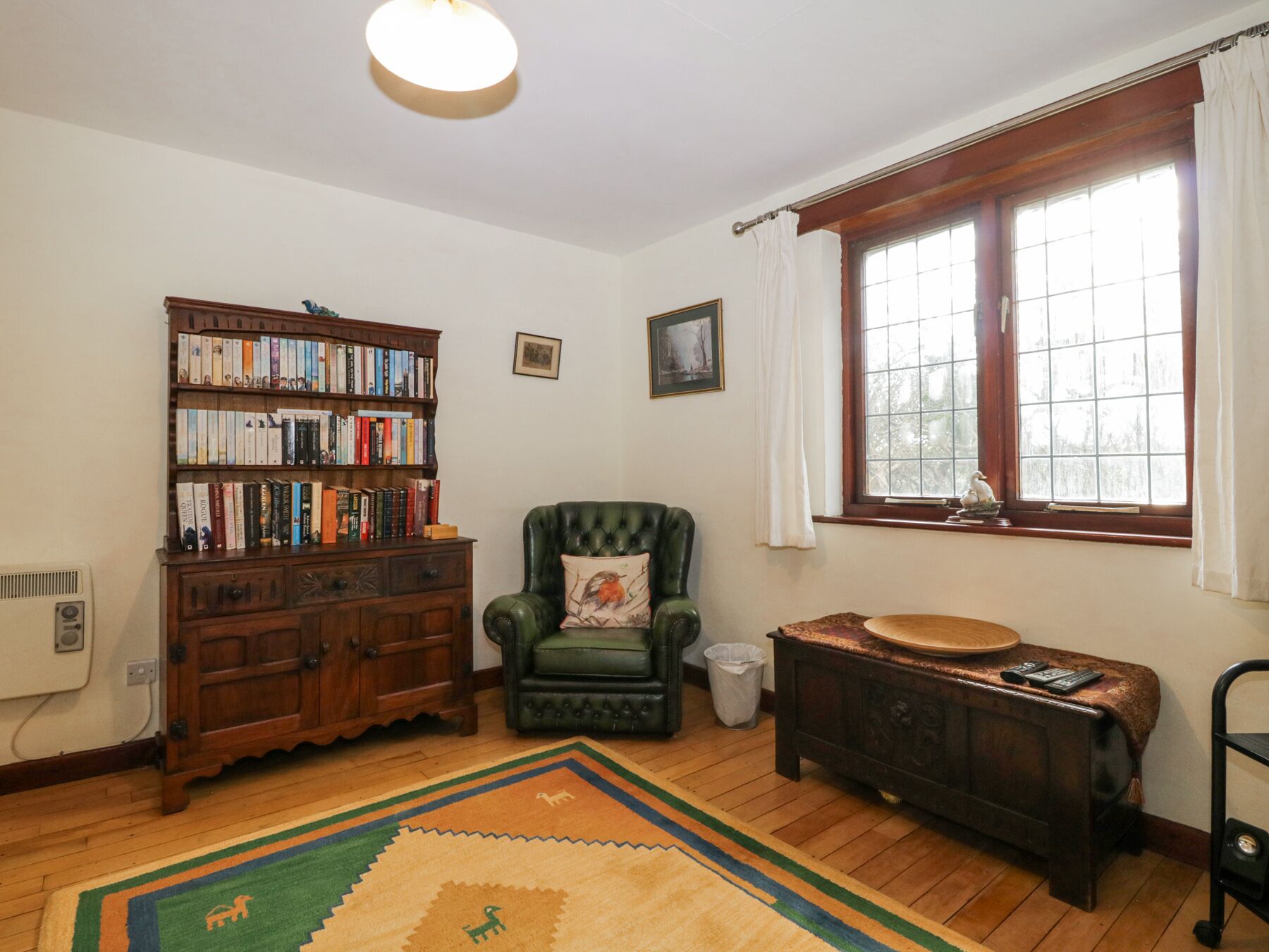 Une pièce chaleureuse avec une bibliothèque en bois, un fauteuil vert, un banc en bois et une fenêtre avec des rideaux.