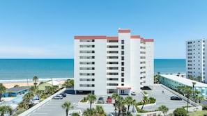 Un hôtel à plusieurs étages avec un parking situé devant, près d’une plage.