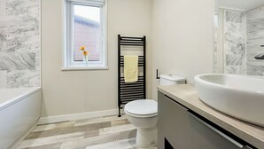 Une salle de bain avec des toilettes blanches, un porte-serviettes noir, un lavabo blanc et une fenêtre donnant sur un beau paysage.