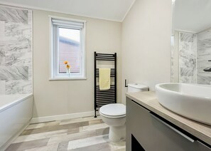 A bathroom with a white toilet, a black towel rack, a white sink, and a window with a view.