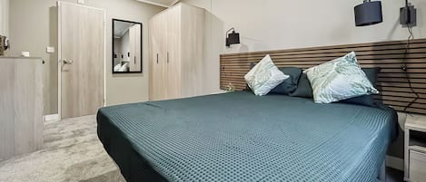 Quarto com cama, guarda-roupa, espelho e mesa de cabeceira.