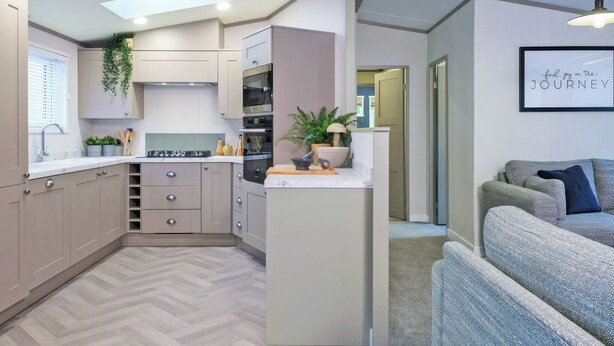 Une cuisine compacte dotée d’appareils électroménagers modernes, d’un plancher à motifs en chevrons et donnant sur un espace de vie avec un canapé et une affiche inspirante.