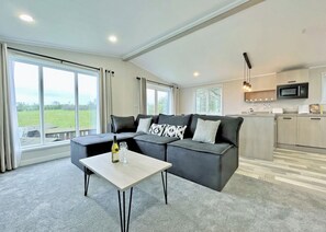 A modern living room with a sectional sofa, a dining table, and a kitchen area with a microwave.