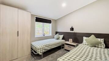 A bedroom with two beds, a wardrobe, a window with a view, and a bedside lamp.