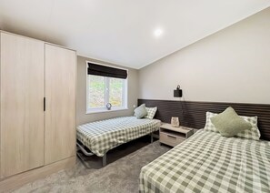 A bedroom with two beds, a wardrobe, a window with a view, and a bedside lamp.