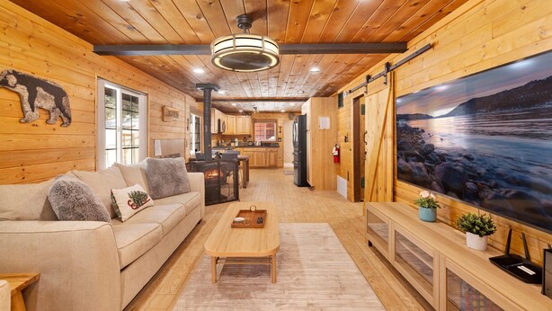Un interior de cabaña acogedor, con detalles de madera, un sofá, una mesa de comedor y un ventanal con vistas panorámicas.