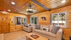 Interior acogedor de una cabaña con paredes de madera, dos sofás, una mesa de centro de madera y una decoración con un oso.