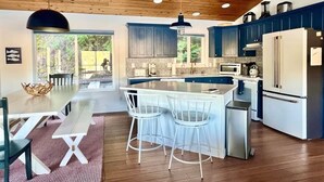 A modern kitchen with wooden ceiling, blue cabinets, white appliances, and a dining area with a bench and chairs. - The Boathouse Large Modern Renovated Waterfront Home with Decks and Docks (Coeur d'Alene)