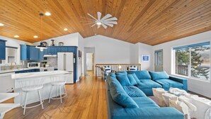 A modern kitchen with wooden ceiling, blue cabinets, and white bar stools. - The Boathouse Large Modern Renovated Waterfront Home with Decks and Docks (Coeur d'Alene)