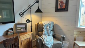 Una habitación acogedora con un sillón de cuero, un escritorio de madera, una lámpara y un cuadro en la pared.