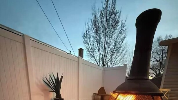 Un patio con un estufa de leña, una cesta tejida con aperitivos y una planta en maceta.