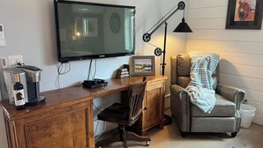 Una sala de estar acogedora con un escritorio de madera, un sillón cómodo, un televisor y una cafetera.