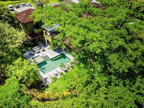 An aerial view of a property with a swimming pool surrounded by lush greenery, a patio area with outdoor furniture, and a building with a tiled roof. - Exclusive Luxury Villa at Reserva Conchal w/ Pool –Just 10 Min Walk to the Beach (Playa Conchal)