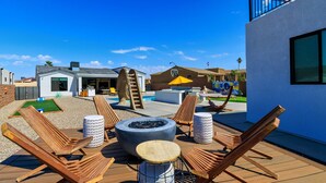 A wooden deck with lounge chairs, a fire pit, and a pool area. - Villa Solara – Ultimate Backyard & Gameroom (Lake Havasu City)