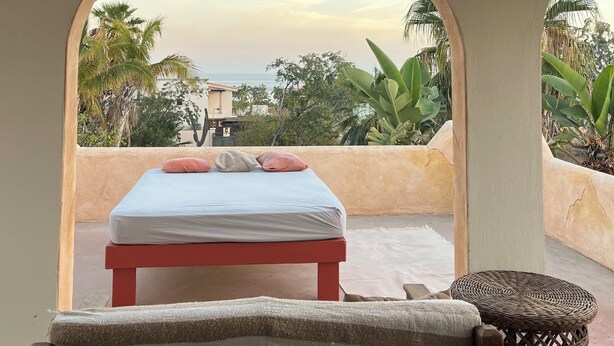 A room with a bed, a small table, and a chair, with a view of palm trees and a building in the background. - Villa El Tule
Beautiful home in the Corridor Area.
Minutes to Chileno Bay (Cabo San Lucas)