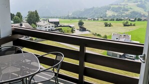 Un balcón con mesa y sillas, con vistas a un valle verde con casas y montañas al fondo.