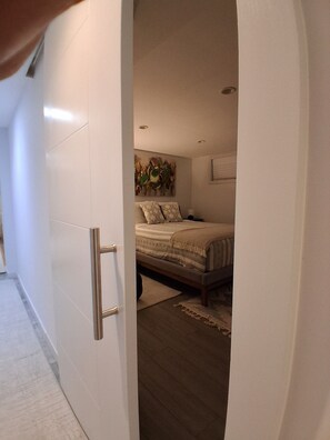 Une chambre à coucher comprenant un lit, une table de chevet, une œuvre d’art accrochée au mur et un luminaire au plafond.