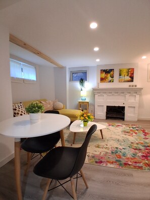 Un salon avec une cheminée, une table à manger avec des chaises, un canapé et un tapis coloré.
