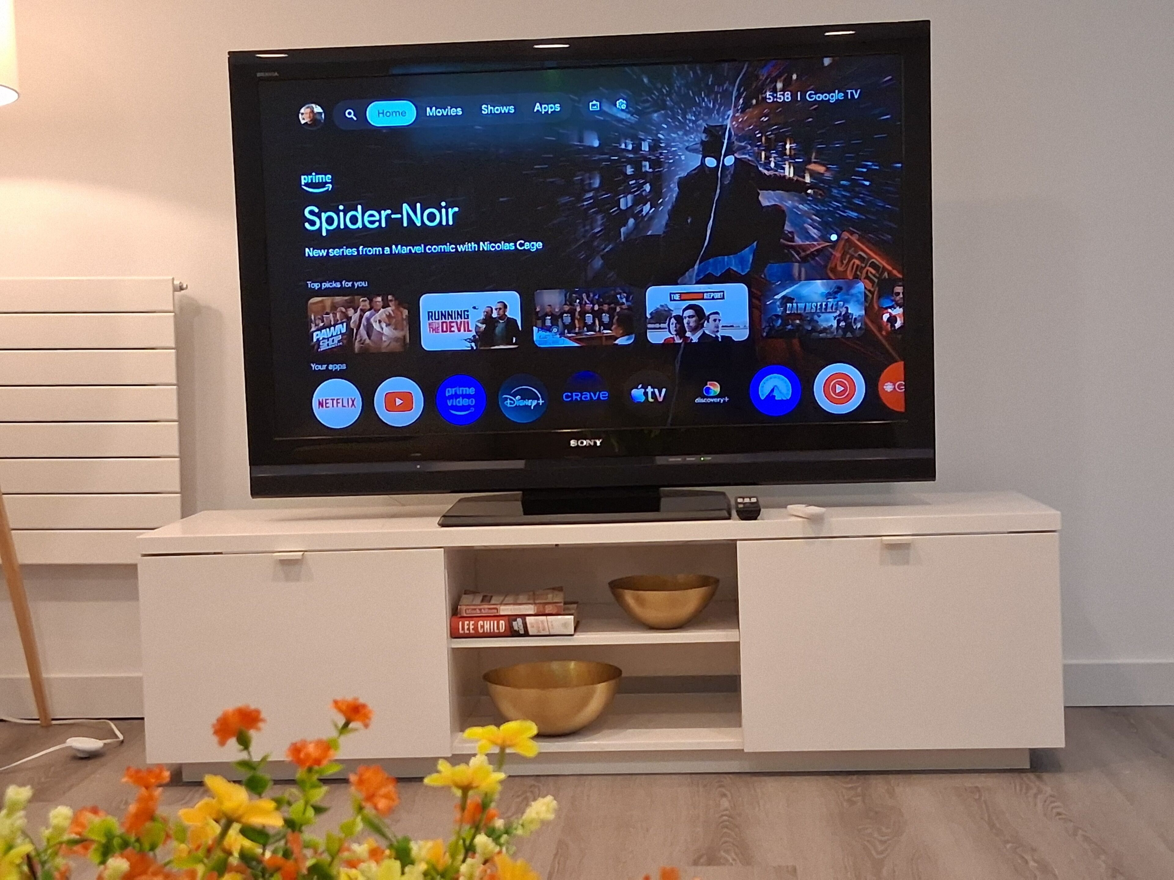 A flat-screen TV on a white entertainment unit with a shelf below displaying books and bowls.