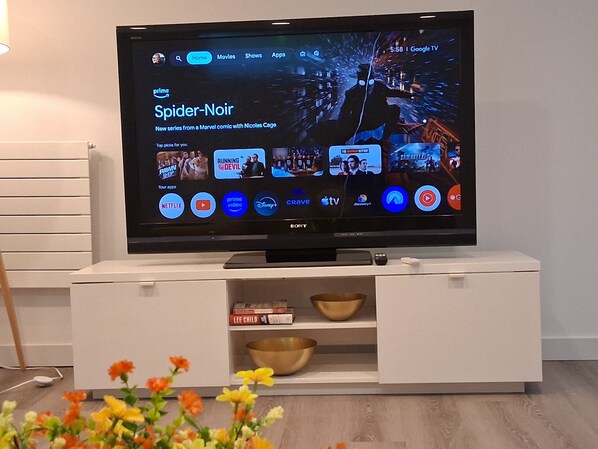 A flat-screen TV on a white entertainment unit with a shelf below displaying books and bowls.