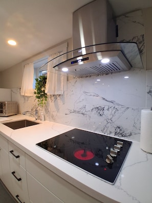 A modern kitchen with a built-in stove, a stainless steel range hood, a marble backsplash, and a white countertop.