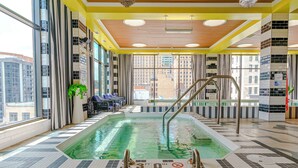 Una amplia piscina interior con 9 metros de profundidad, rodeada de suelo y paredes con azulejos, y vistas a edificios exteriores.