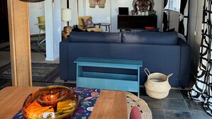 Una sala de estar con un sofá azul, una mesa de comedor de madera y una lámpara colgante.