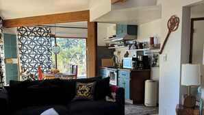 Una sala de estar con un sofá negro, una mesa de centro redonda de madera y un tapete estampado.