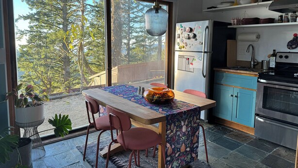 Una cocina moderna con un ventanal grande, una mesa de comedor con sillas y vistas a árboles.
