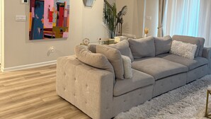A modern living room with a beige sectional sofa, a fluffy rug, and a colorful abstract painting on the wall. - Charming 3-bedroom townhome with loft, WiFi and AC in peaceful Lawrenceville (Lawrenceville)