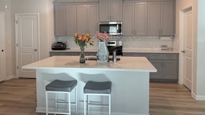 A modern kitchen with grey cabinets, a stainless steel microwave, and a central island with two stools. - Charming 3-bedroom townhome with loft, WiFi and AC in peaceful Lawrenceville (Lawrenceville)