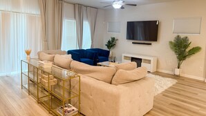 A living room with a beige sectional sofa, a blue couch, a glass coffee table, and a ceiling fan. - Charming 3-bedroom townhome with loft, WiFi and AC in peaceful Lawrenceville (Lawrenceville)