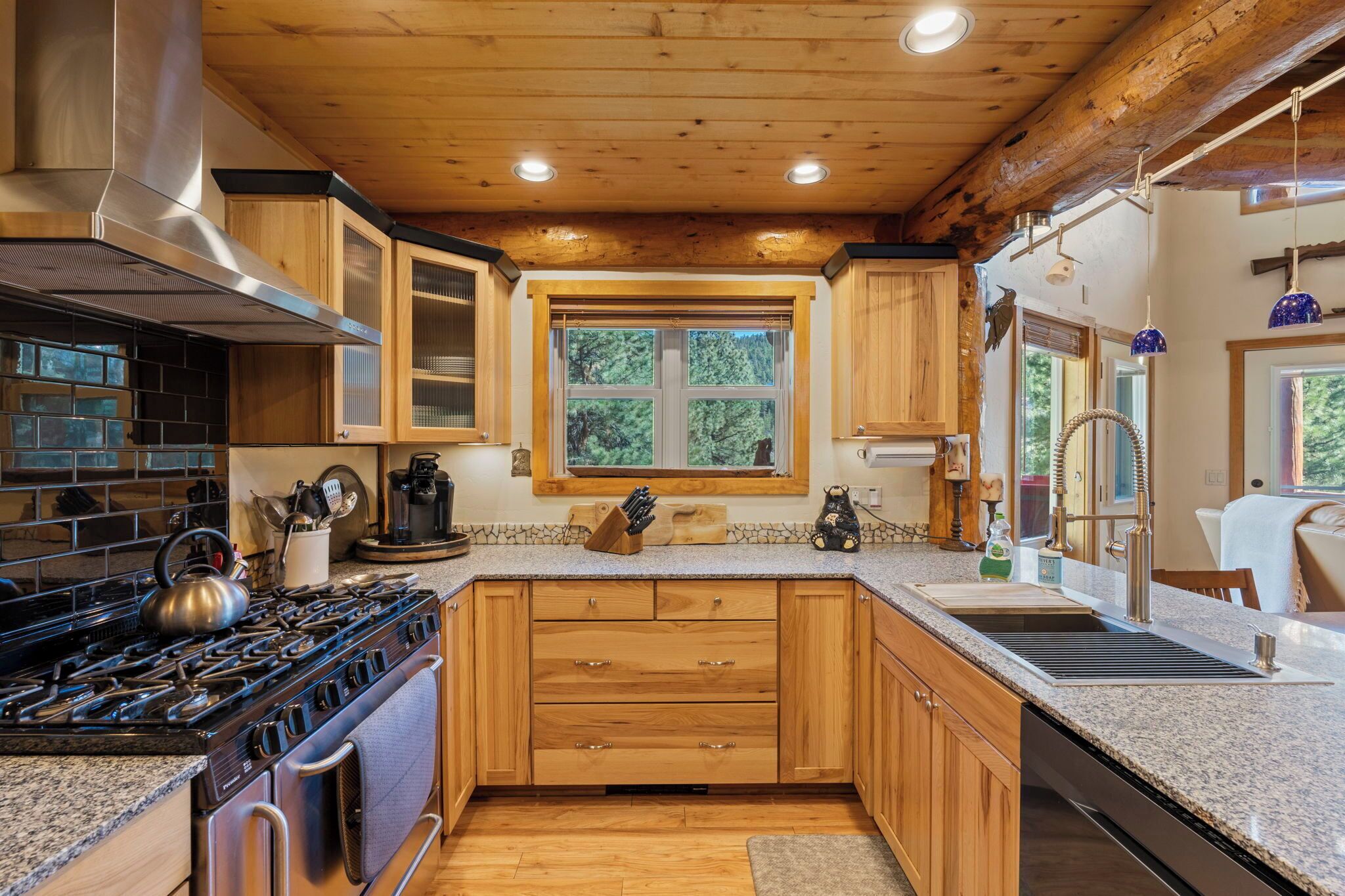 A modern kitchen with wooden cabinets, granite countertops, a stainless steel range hood, and a large window providing natural light.