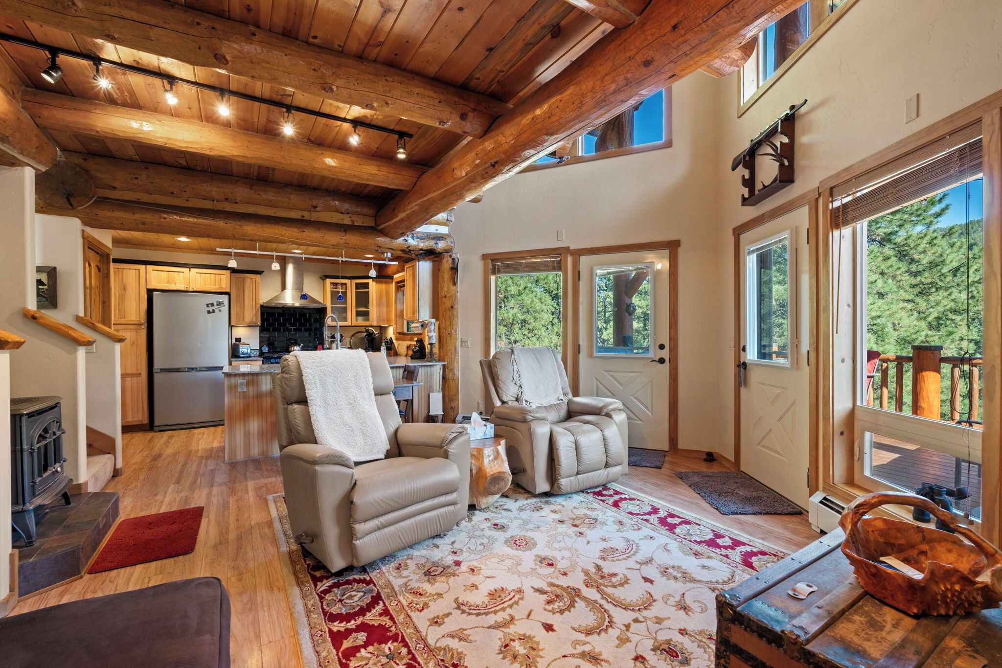 A spacious living room with a fireplace, two leather armchairs, a large patterned rug, and a view of the outdoors through large windows.