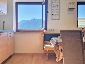A small kitchen with a window overlooking a mountain range, a wooden chair, and a table with a tablecloth.