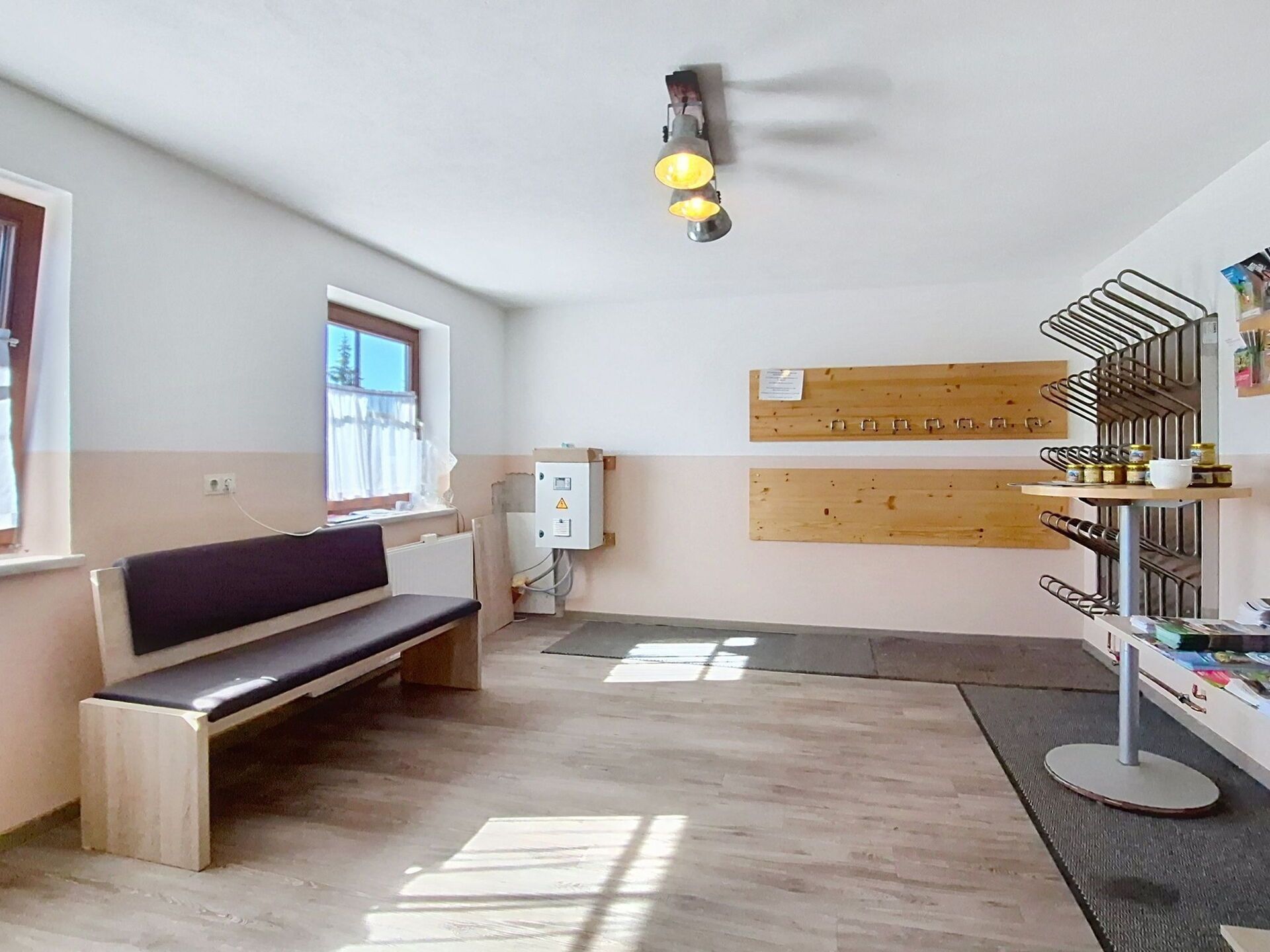Una habitación con un banco, un estante con frascos y una ventana con cortinas.