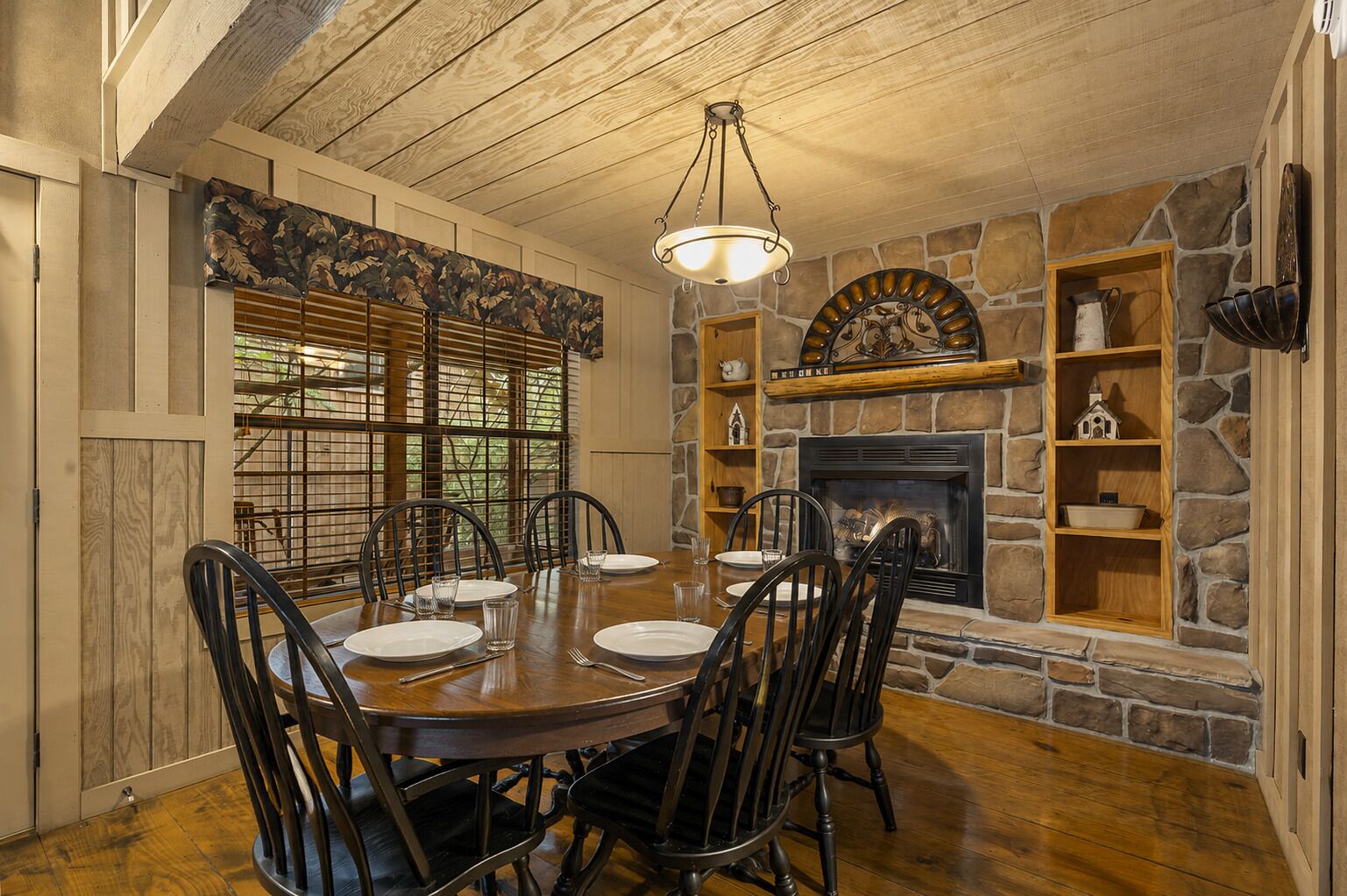 A dining room with a stone fireplace, wooden dining table, and chairs.