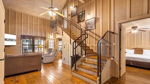 A wooden-paneled room with a staircase, a sofa, a chair, and a bed. - Relaxing Branson Cabin Getaway (Branson)
