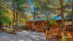 A wooden cabin with a covered porch, surrounded by trees and a stone pathway. - 🏡 2BR Branson Cabin Retreat | Pools, Hot Tub, Pet-Friendly (Branson)
