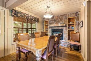 Une salle à manger avec une table et des chaises en bois, une cheminée en pierre et une bibliothèque.