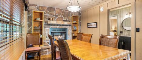 A dining area with a wooden table and chairs, a stone fireplace, and built-in shelves.