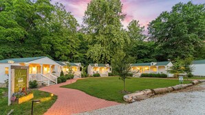 A row of cottages with a red brick pathway leading to the entrance, surrounded by lush greenery.