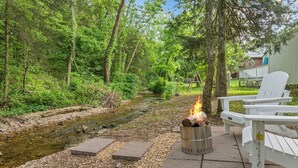 A riverside patio with a fire pit and Adirondack chairs.