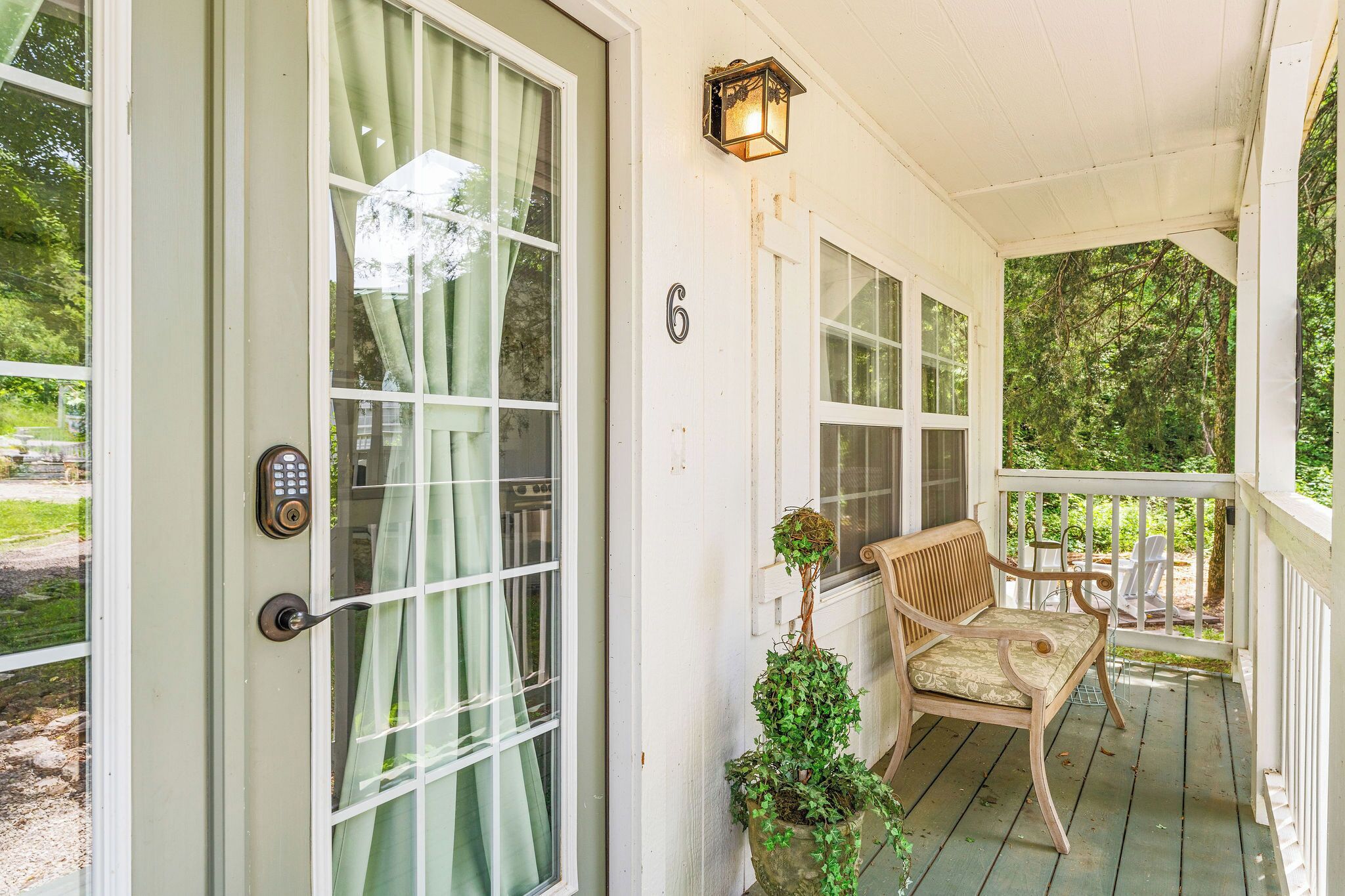 A porch with a bench, a potted plant, and a door with a number.