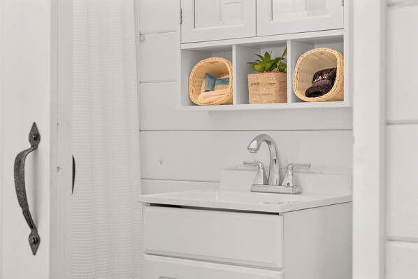 A bathroom with a white sink, a silver faucet, and wicker baskets on a shelf.