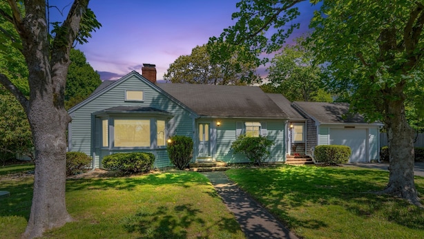 Ein eingeschossiges Haus mit Veranda, Garage und gepflegtem Rasen.