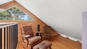 A small attic room with a sloped ceiling, wooden floor, a radiator, two chairs, and a small table. - Family & Pet-Friendly Cape Escape Near Beach (Hyannis)