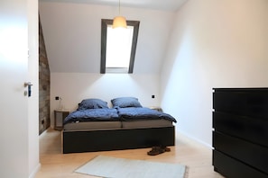 Une chambre à coucher comprenant un lit, une commode, une table de chevet, une lampe suspendue et une fenêtre.