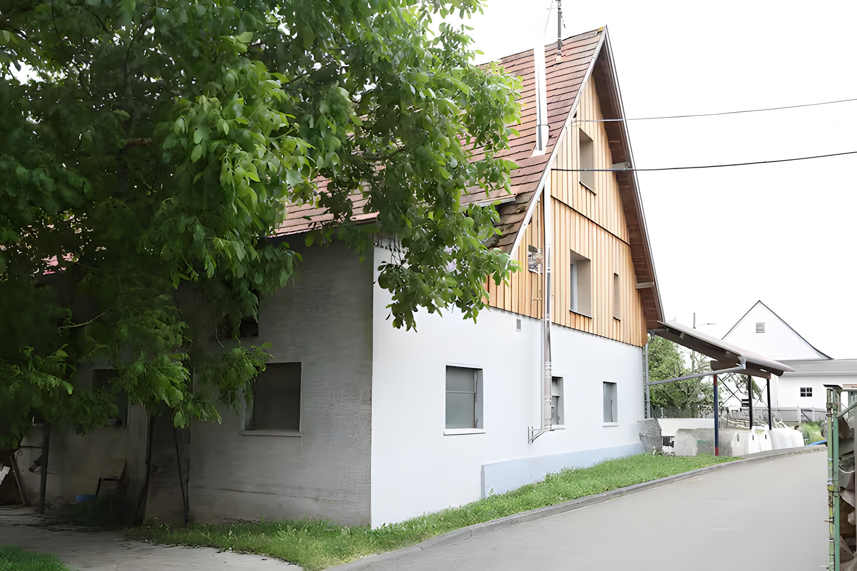 Ein modernes Haus mit einem geneigten Dach, ein großer Baum davor und ein gepflasterter Auffahrt.